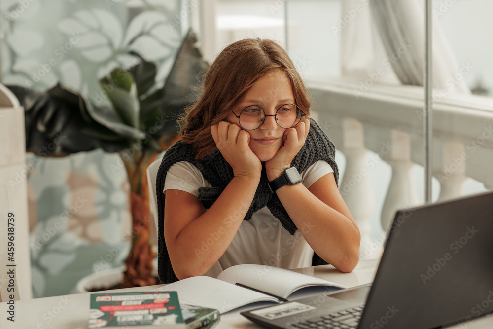 A teenage girl with glasses frowns at a laptop A teenage girl with glasses frowns at a laptop