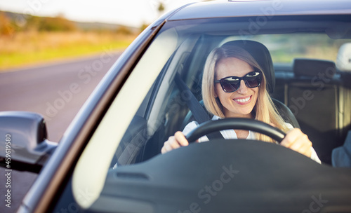 Happy mature woman in sunglasses and business wear enjoying driving her modern car. View of female driver through windshield. Confidence on road.