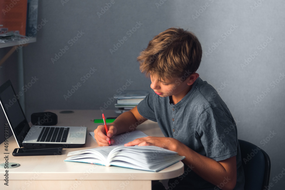 student teenager boy doing homework with laptop, open copybook and computer, workplace at home student teenager boy doing homework with laptop, open copybook and computer, workplace at home