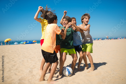Excited preteen boy friends rejoicing after game at beach. Multiethnic kids hugging and shouting when playing football. Summer vacation, friendship concept