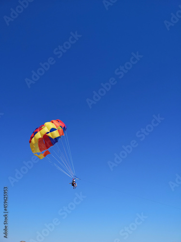 Young couple is flying in the blue sky using a colorful parachute. parasailing