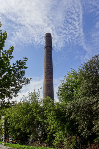 Tall old brown chimney of Kultuurikatel with bright blue with white clouds sky. Many green trees around. Tallinn, Estonia, Europe. September 2021