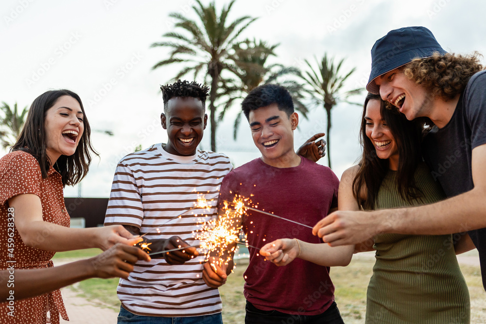 © Xavier Lorenzo - Happy multiracial people laughing and having fun together with sparkles outdoors - Young friends celebrating new year eve - Friendship and millennial eve celebration