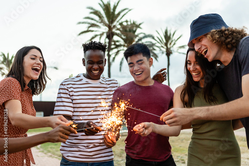 Happy multiracial people laughing and having fun together with sparkles outdoors - Young friends celebrating new year eve - Friendship and millennial eve celebration photo