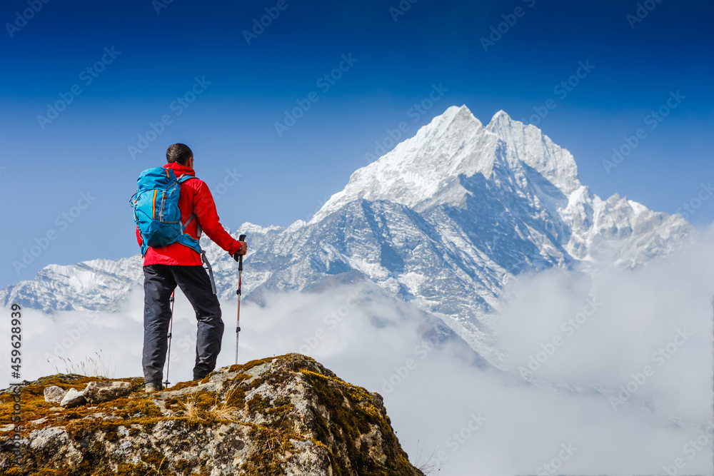 Hiker with trekking poles stands on the slope against the background of high snow-capped mountains