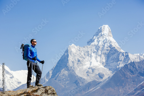 Hiker with trekking poles stands on the slope against the background of high snow-capped mountains