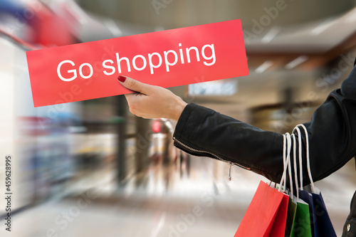 woman's hand holds shopping bags and a sign that says go shopping. The concept of shopping and shopaholism. photo