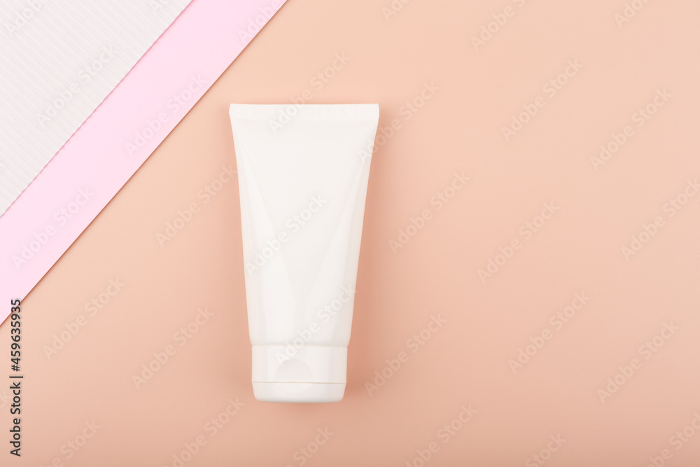 Creative elegant flat lay with white cream tube with face or hand cream or lotion on bright pastel beige background decorated with white and pink paper. Concept of beauty products for skin care Creative elegant flat lay with white cream tube with face or hand cream or lotion on bright pastel beige background decorated with white and pink paper. Concept of beauty products for skin care