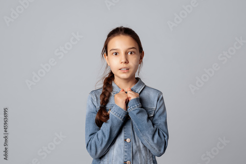 preteen girl looking at camera with nervous and scared facial expression, isolated on grey background, wearing in denim jacket