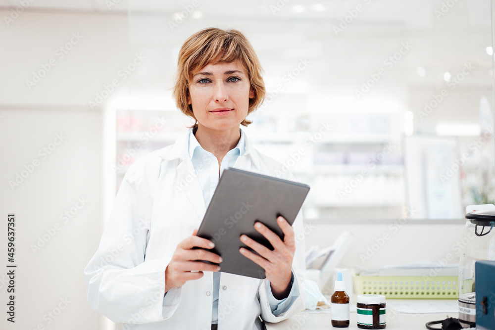 Female pharmacist with digital tablet standing in pharmacy