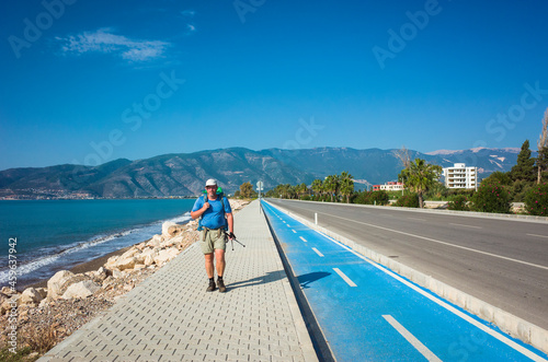 Hiking on Lycian way trail. Man with backpack trekking along Finike long beach on walkway next to road  Mediterranean coast of Turkey