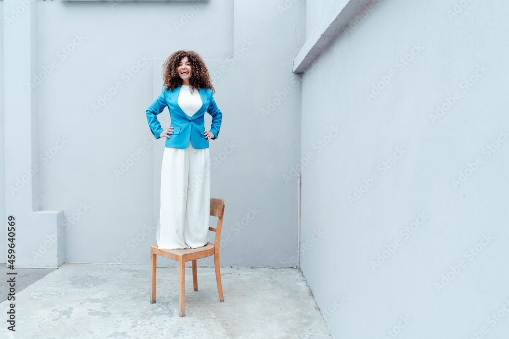 Happy female professional standing with on chair in front of gray wall Happy female professional standing with on chair in front of gray wall
