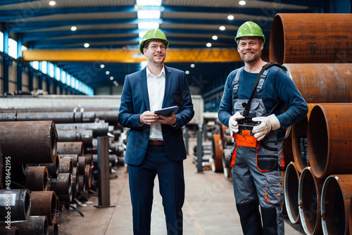 Smiling male manager standing with warehouse worker in factory photo