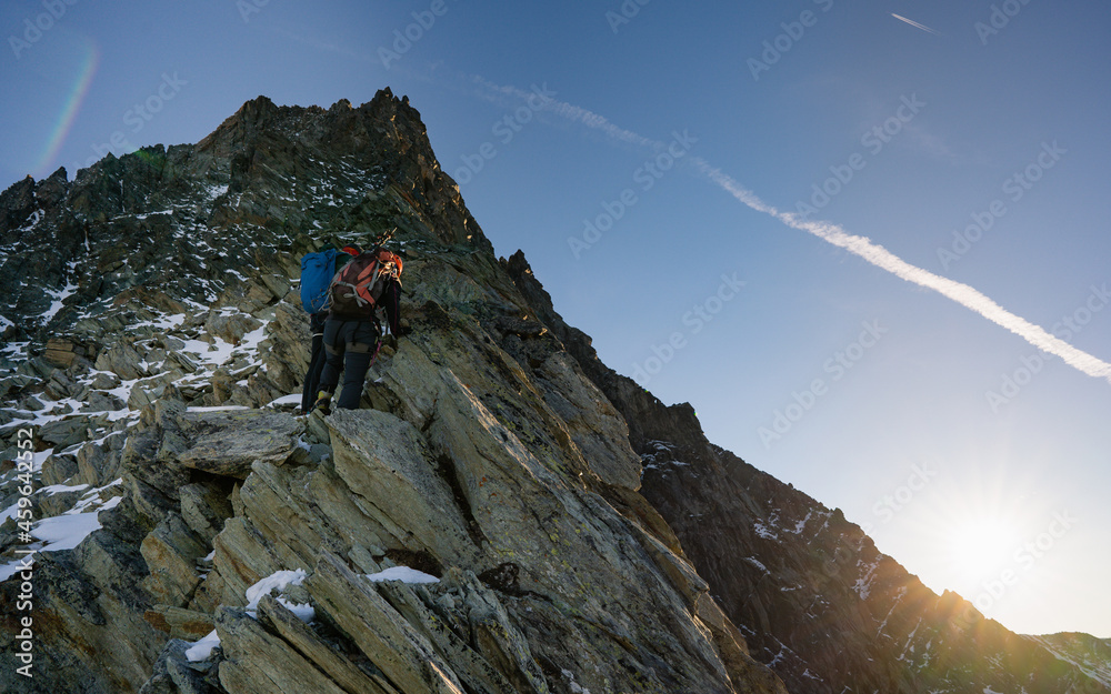 Back view of rock climbers with backpacks using fixed rope while ascending high rocky mountain. Male mountaineers climbing natural rock formation and trying to reach mountaintop.