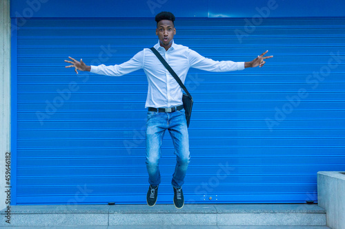 portrait african american man jumping happy with white shirt and briefcase on blue background looking at camera © luisrojasstock