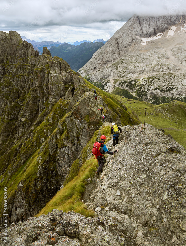 Kletterer unterwegs auf dem schmalen Grat im Trinchee Klettersteig in Südtirol, Italien mit Marmolata im Hintergrund