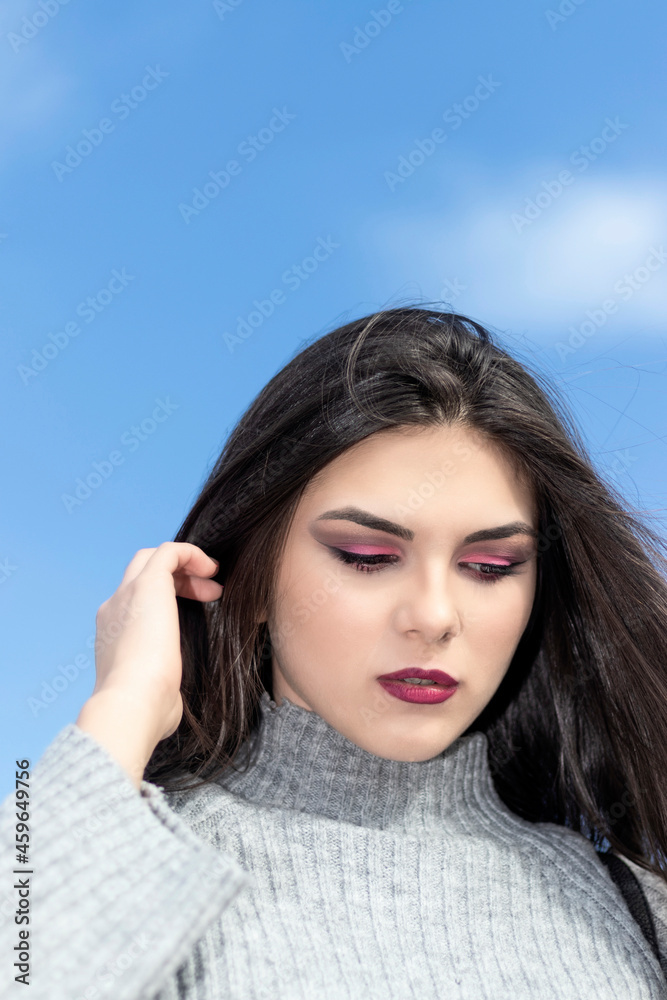 Fototapeta premium brunette woman looking down with l amno in her hair and a gray woolen dress and blue sky in the background