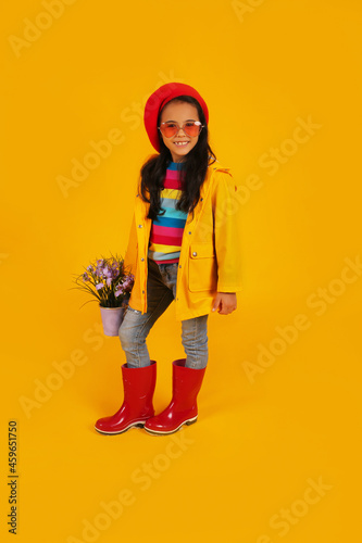 a dark-skinned girl in a red beret, pink heart-shaped glasses, a yellow raincoat, and a bucket with flowers in her hands