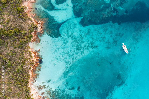 Fototapeta Naklejka Na Ścianę i Meble -  View from above, stunning aerial view of a green and rocky coastline with a sailboat sailing on a turquoise, crystal clear water. Liscia Ruja, Costa Smeralda, Sardinia, Italy..