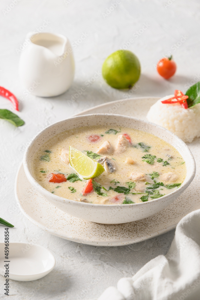 Spicy creamy coconut Tom Kha Gai soup with chicken, coconut milk, galangal, lemongrass,mushrooms on light background. Asian Thai food. Vertical format. Coconut Chicken Soup.