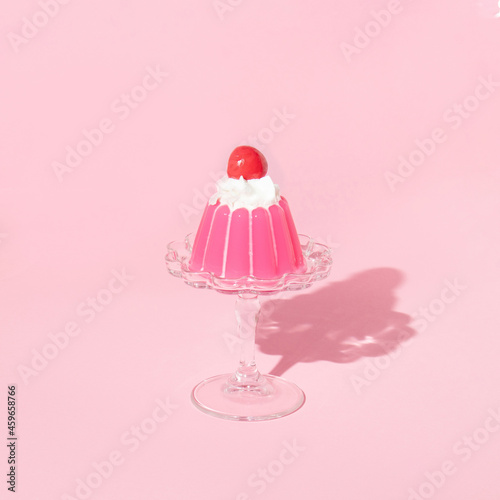 Pink jello on dish with cherry on top on pastel pink background. 70s or 80s retro style aesthetic dessert idea. Minimal food concept. photo