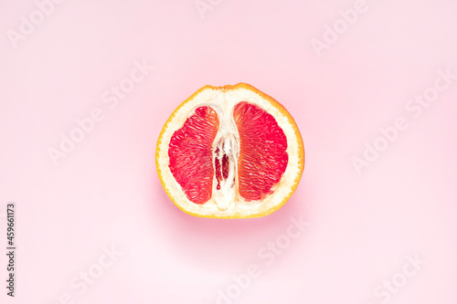 Half of fresh grapefruit on pink background. Symbol of vagina. Gynecology, female intimate health, menstruation concept. photo