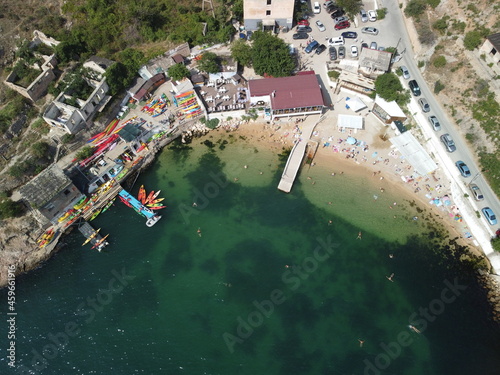 Aerial drone view on colorful kayaks grouped at a dock in sea bay. Group of happy kayakers are walking or training with instructor at sea bay. Active sea vacations concept