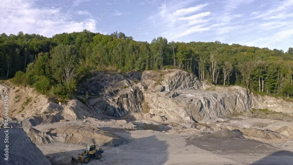 Granite quarry cut out of hill in the forest with front end loader in the foreground