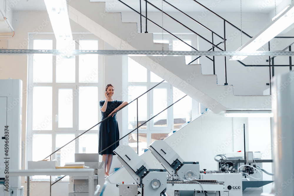 Female professional talking on mobile phone while standing on steps in workshop Female professional talking on mobile phone while standing on steps in workshop