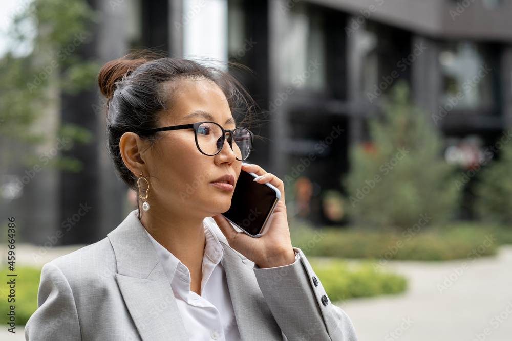 Young serious Asian businesswoman with smartphone by ear calling business partner Young serious Asian businesswoman with smartphone by ear calling business partner