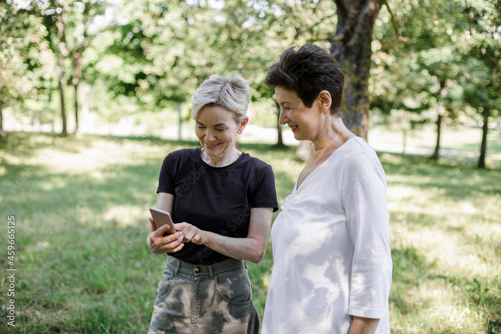 Woman using mobile phone while standing by friend at park Woman using mobile phone while standing by friend at park