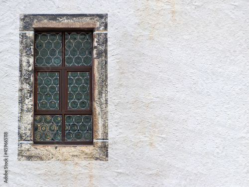 old leaded glass transom window with stone surround and a light colored, textured plastered house wall with copy space to the right