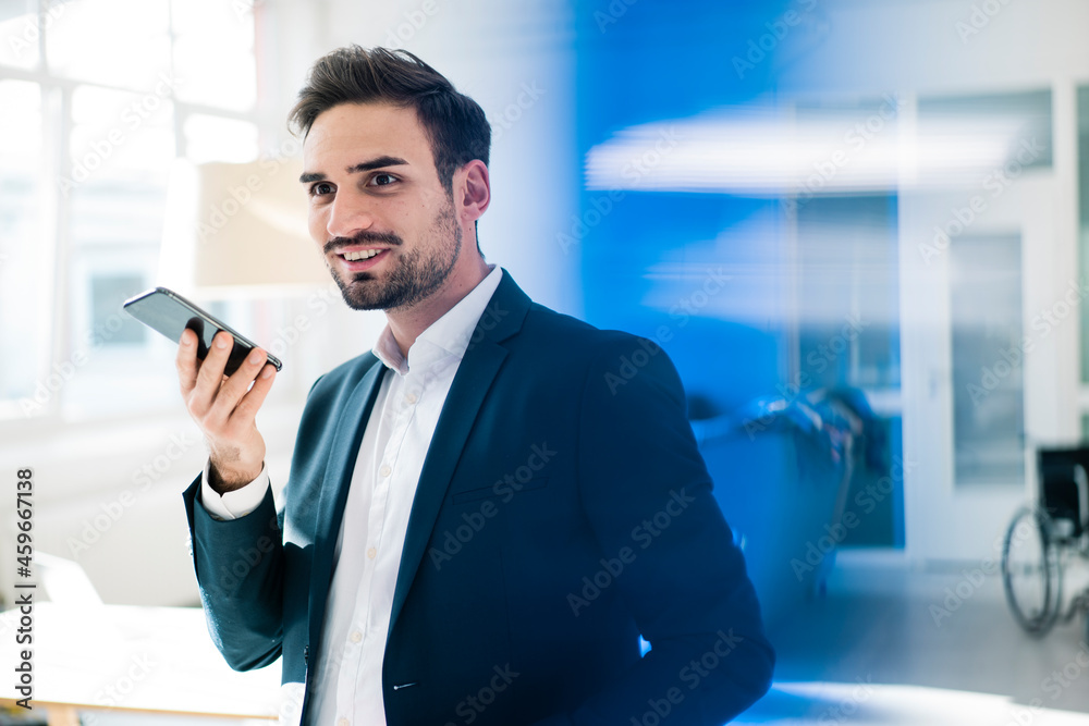 Smiling young male professional talking on mobile phone through speaker in office Smiling young male professional talking on mobile phone through speaker in office