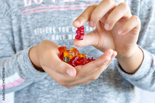 A girl holds a gummy bear in her hand, wants to eat jelly sweets. Close-up. Concept of children's delicacy, unhealthy food, vitamins for kids.