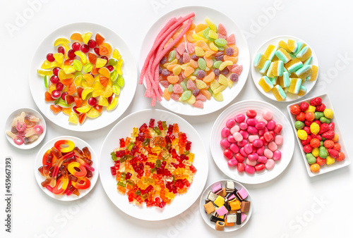 Many different jelly candies on plates on a white background. Top view.