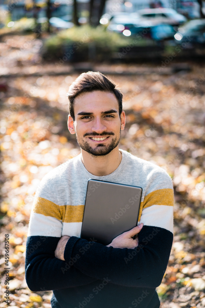 Happy handsome man holding digital tablet while standing with arms crossed at park Happy handsome man holding digital tablet while standing with arms crossed at park