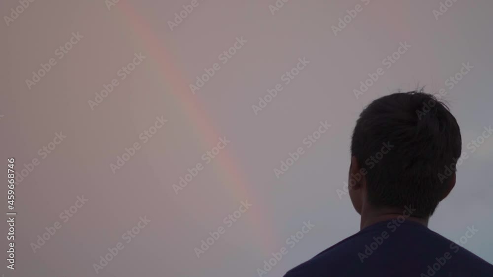 Portrait of a young Indian looking at the rainbow. Happy kid looks towards the rainbow. Kid is happy to see rainbow for first time and is excited and amazed to see it.
