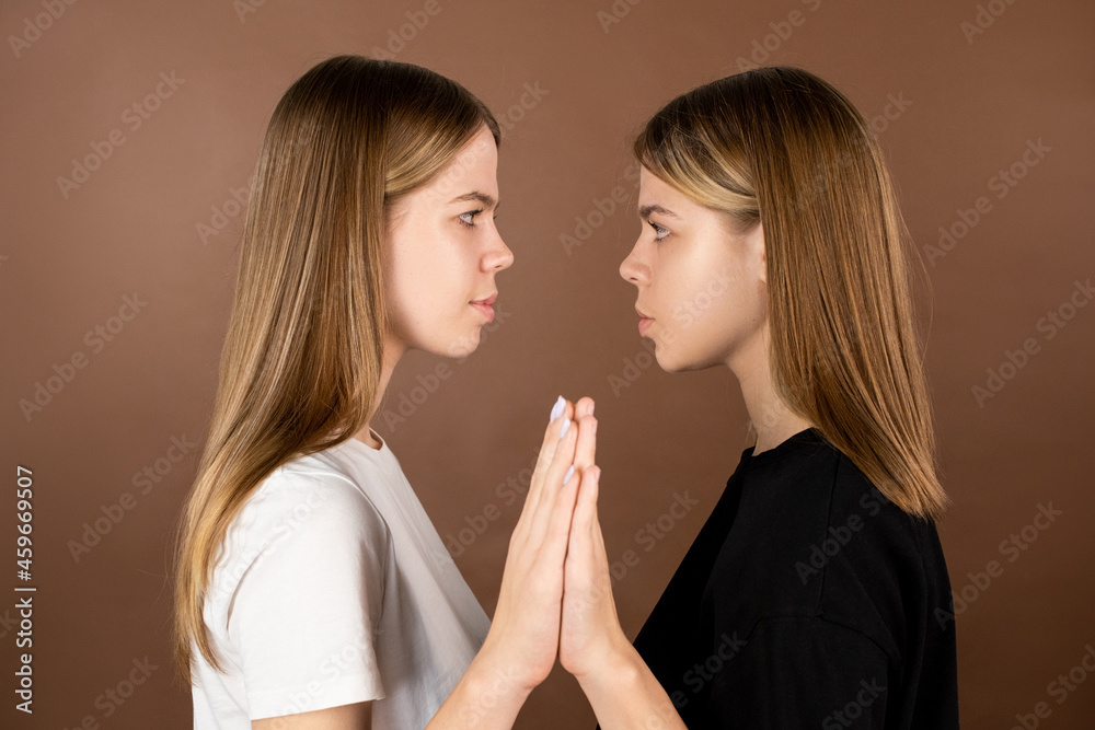 Side view of twin teenage girls touching by hands and looking at one another - obrazy, fototapety, plakaty 