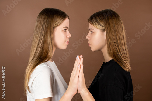 Side view of twin teenage girls touching by hands and looking at one another photo