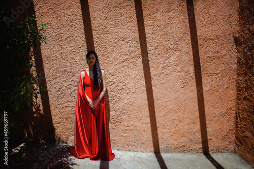 Mature woman wearing red cape and dress standing in front of wall photo