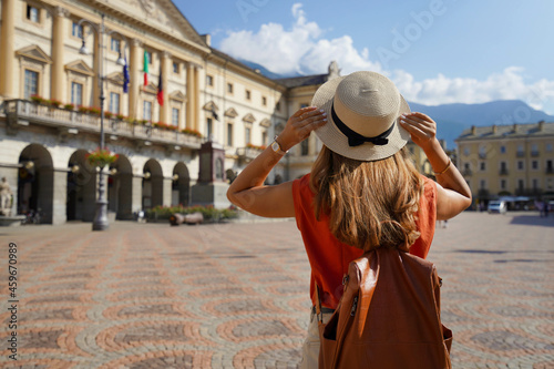 Stylish traveler woman holds hat on sunny day in Aosta city, Italy