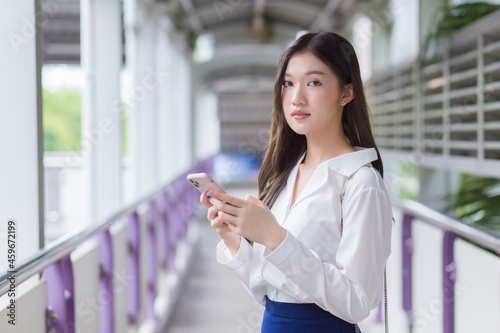 Asian beautiful business female stands on flyover of skytrain in town while uses her smartphone to send messages to customers.