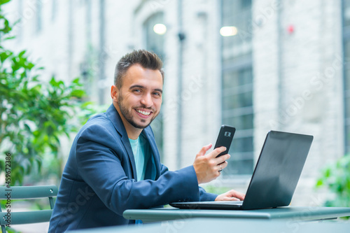 Young successful caucasian businessman works in an outdoor cafe using a computer. Business, freelance and remote work.