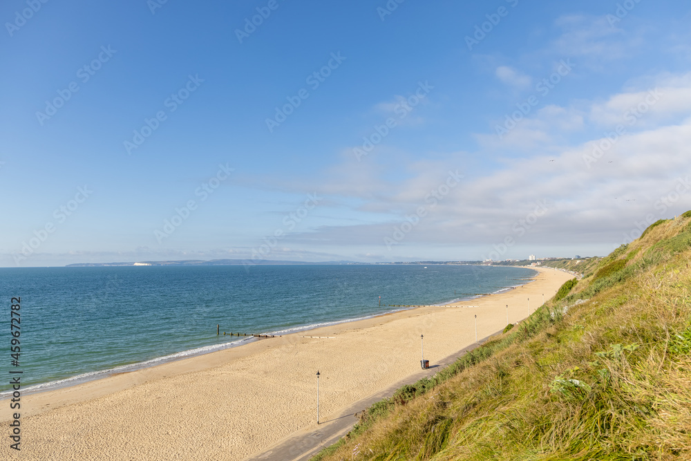 A scenic majestic view of  Bournemouth bay with sandy beach from a grassy cliff under a beautiful blue sky and some white clouds