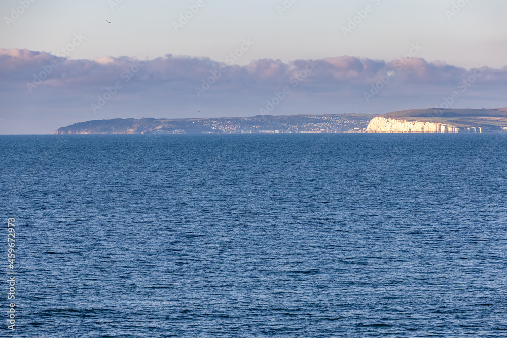 A scenics majestic view of the sea from the sea with white cliff and hill in the background under a beautiful blue sky and some low white clouds