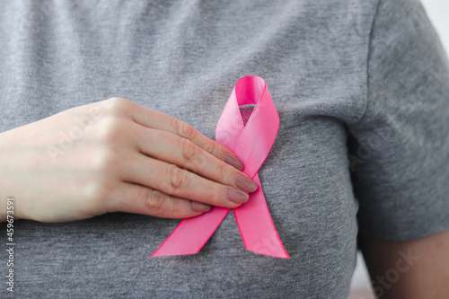 Woman in gray t-shirt attaches pink ribbon to her chest. Breast Cancer Awareness Month. Promoting campaign against cancer.
