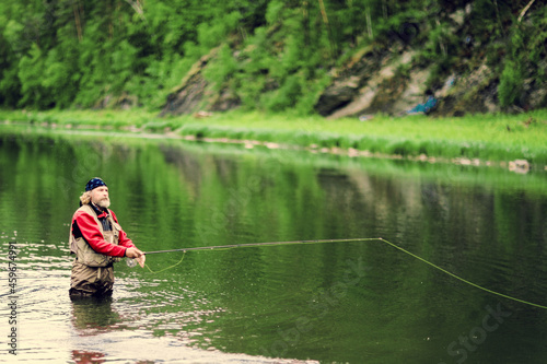 Fishing on the lake. A man in a bandana holds a fishing rod and stands with his feet in the water. Fisherman fishing in the river. Fly fishing.