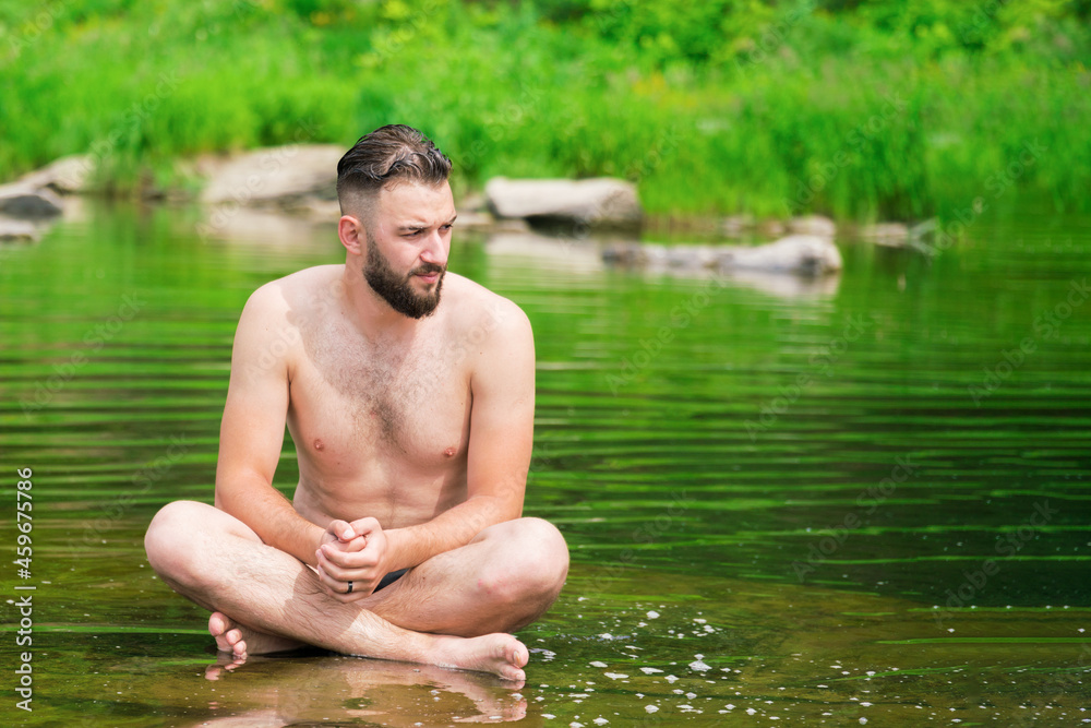 A man meditates in the lotus position, sitting on a stone in the middle of a mountain river. Meditation and peace.. A man meditates in the lotus position, sitting on a stone in the middle of a mountain river. Meditation and peace..