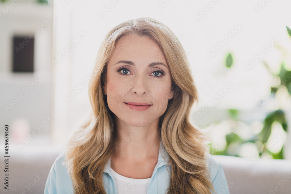 Photo of adorable cute age woman dressed blue shirt sitting sofa smiling indoors home room Photo of adorable cute age woman dressed blue shirt sitting sofa smiling indoors home room