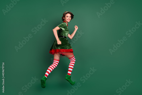 Photo of energetic lady jump hurry wear elf costume hat striped socks isolated green color background